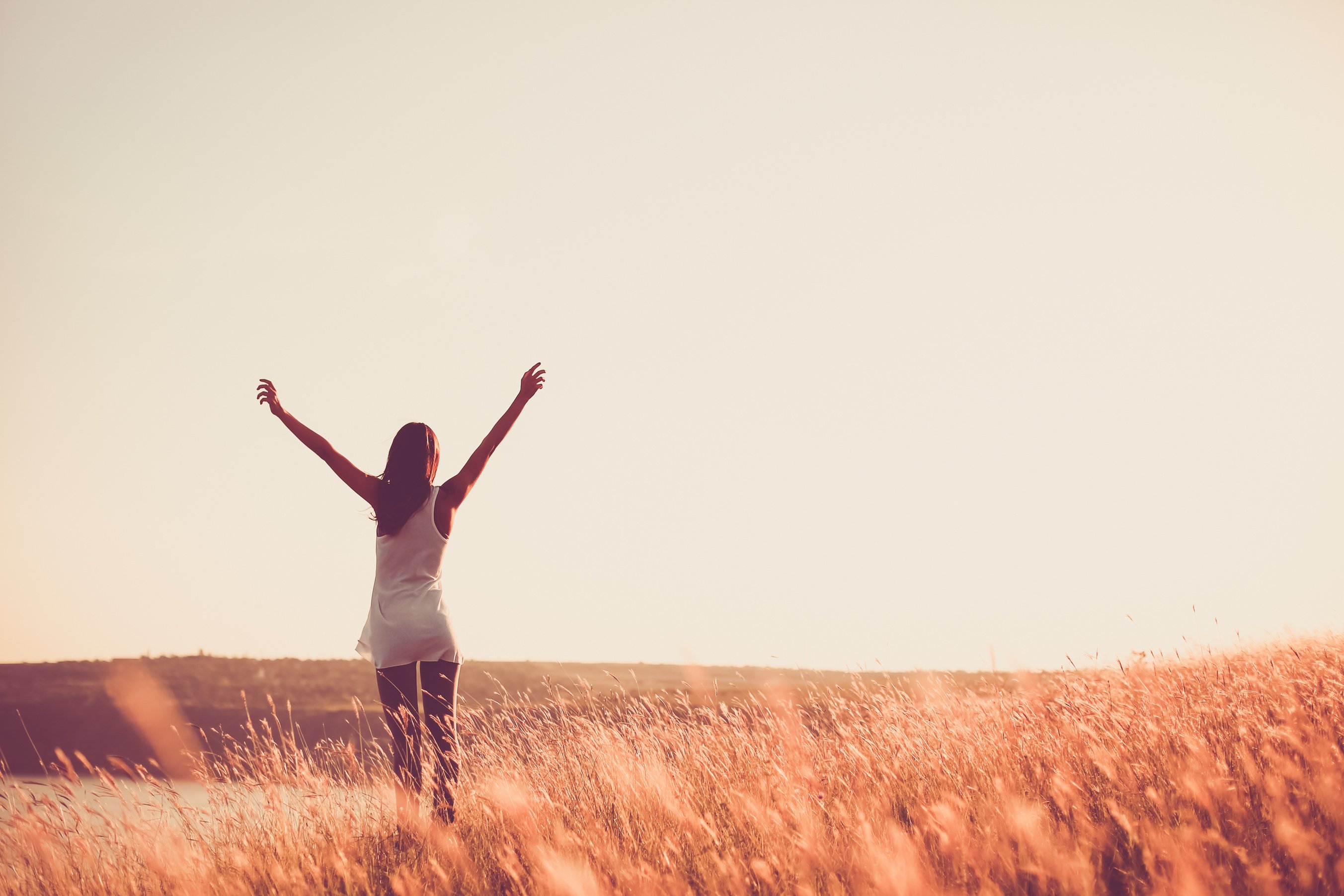 Free woman raising arms to golden sunset